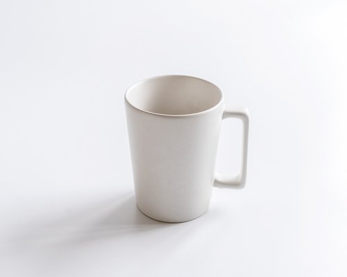 Minimal clean white ceramic mug containing warm tea on a work surface