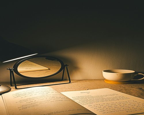 A warm desk lamp neatly highlighting an open paper book page on a cozy table setup